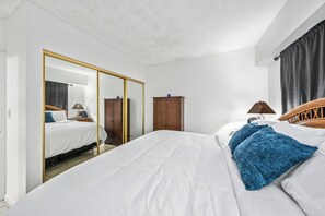 A bedroom with a large bed, a wardrobe, a mirror, and a window with curtains.