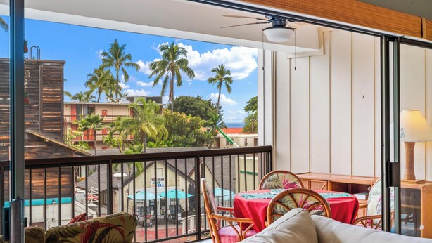 A balcony with a view of palm trees and buildings, a table with chairs, and a sofa.