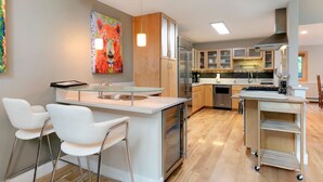 Una cocina moderna con una isla central, taburetes de bar, electrodomésticos de acero inoxidable y un cuadro abstracto colorido en la pared.