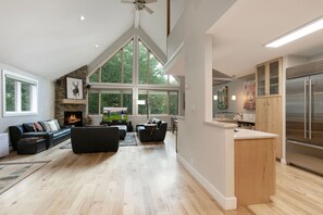 A spacious living room with a fireplace, a large window, and a kitchen area with a refrigerator. - 27 Bachelors Gulch Road 5 Bedroom Home by RedAwning (Avon)
