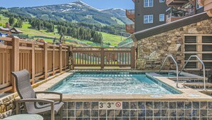 Un espace piscine avec vue sur les montagnes, des chaises longues en bois et un bâtiment en pierre.