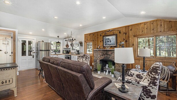 A cozy cabin interior with a wooden interior, a stone fireplace, a sofa, a dining table, and a kitchen area. - Niwot Cabin - Stay In Rocky Mountain National Park - Estes Park - New Listing - 22-zone3298 2 Bedroom Cabin by RedAwning (Estes Park)