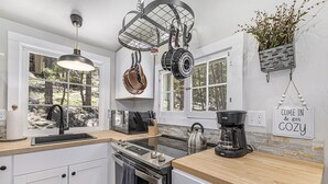 A modern kitchen with white cabinets, a wooden countertop, hanging pots, a kettle, and a coffee maker. - Niwot Cabin - Stay In Rocky Mountain National Park - Estes Park - New Listing - 22-zone3298 2 Bedroom Cabin by RedAwning (Estes Park)