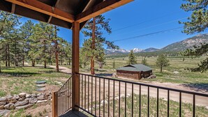 A wooden deck with a metal railing overlooking a mountainous landscape with a small cabin. - Niwot Cabin - Stay In Rocky Mountain National Park - Estes Park - New Listing - 22-zone3298 2 Bedroom Cabin by RedAwning (Estes Park)