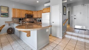 A kitchen with wooden cabinets, a granite countertop, a refrigerator, and a microwave.