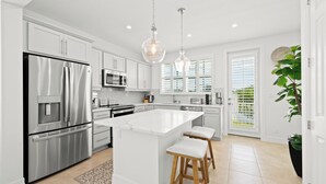 A modern kitchen with stainless steel appliances, a large island with stools, and pendant lighting. - Canalfront Home! Near Anna Maria Island (Cortez)