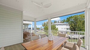 A covered outdoor patio with a wooden table and wicker furniture, overlooking a body of water and a dock. - Canalfront Home! Near Anna Maria Island (Cortez)