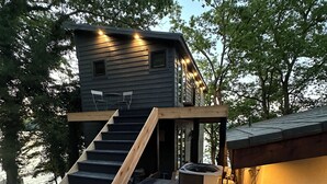 Ein modernes Blockhaus mit einer Holztreppe, die zu einer Terrasse führt, einem Außenheizer und Blick auf die umliegenden Bäume.