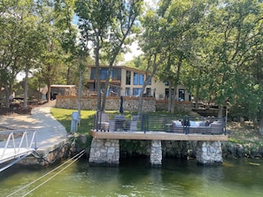 A lakeside property with a stone dock, outdoor seating, and a large house with multiple levels and balconies. - Unique home and 3 level bunkhouse.  Lake of the Ozarks. Accommodate 24 guests!   (Gravois Mills)
