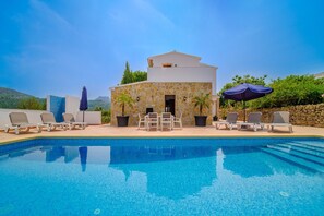 A poolside area with a stone building, lounge chairs, and umbrellas. - Villa La Sella With Private Pool, Terraces and Mountain View (Pedreguer)