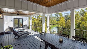 A covered outdoor deck with a table and chairs, overlooking a lake and forest.