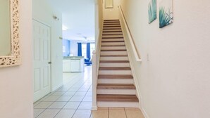 Un escalier menant à un deuxième étage, avec une porte blanche sur la gauche et un coin cuisine au fond.