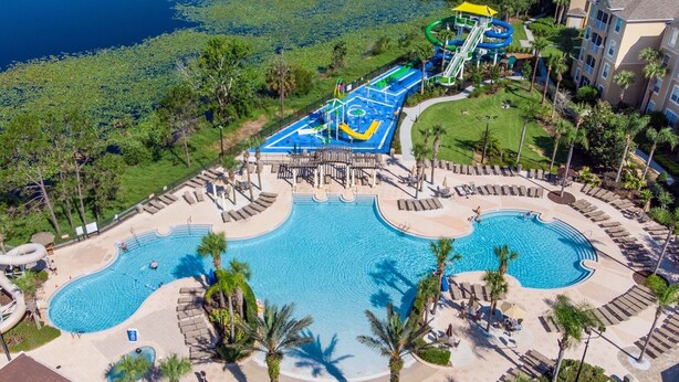 Vue aérienne d’un complexe hôtelier doté d’une grande piscine centrale, d’un parc aquatique avec des toboggans et une rivière à courant doux, ainsi que de plusieurs espaces de détente agrémentés de palmiers.