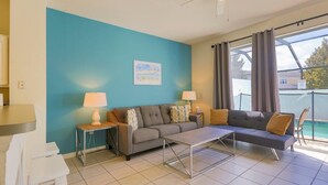 Un salon moderne comprenant un canapé, deux tables d’appoint avec des lampes, une table basse et une vue sur une piscine, visible à travers de grandes fenêtres.