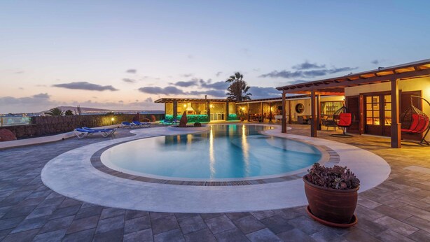 Ein Pool mit Liegestühlen, einer überdachten Lounge und Blick auf die Stadt bei Dämmerung.