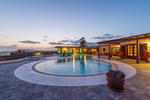 A swimming pool with lounge chairs, a covered seating area, and a view of the cityscape at dusk. - Villa Deseo Sol - Five Bedroom Villa, Sleeps 10 (Playa Blanca)
