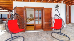 Deckenbalken aus Holz, ein Schlafzimmer mit Bett und Ausblick sowie zwei rote Stühle mit Korbsitze.