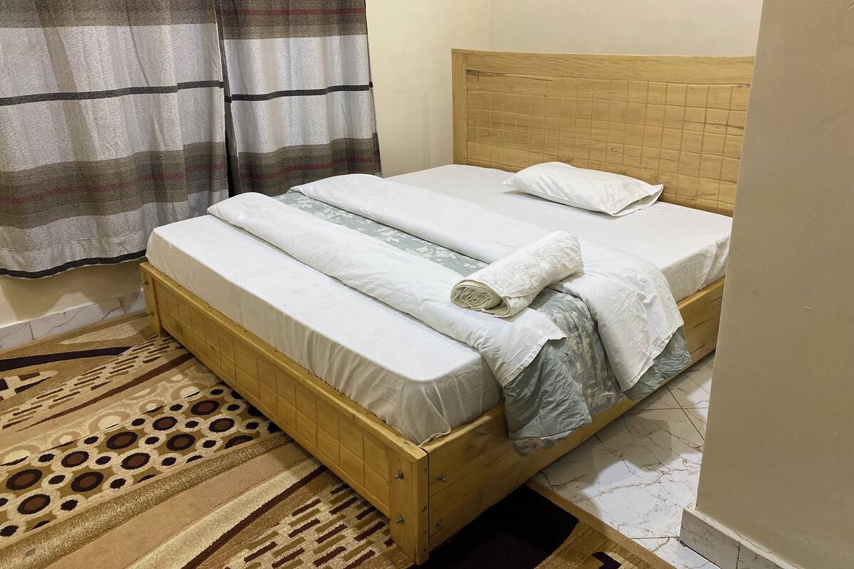 A single bed with a wooden frame, a headboard, and a patterned rug.