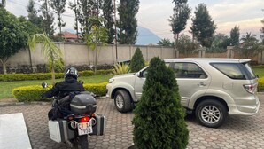 A paved area with a motorcycle, a silver SUV, and a small tree in a planter. - Virunga House (Muhoza)