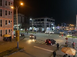 Escena nocturna de una calle urbana con edificios, vehículos y peatones.