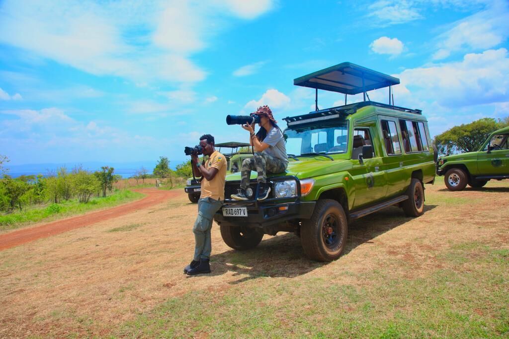 A green vehicle with a roof rack and a license plate, parked on a dirt road with a clear sky and sparse vegetation in the background.