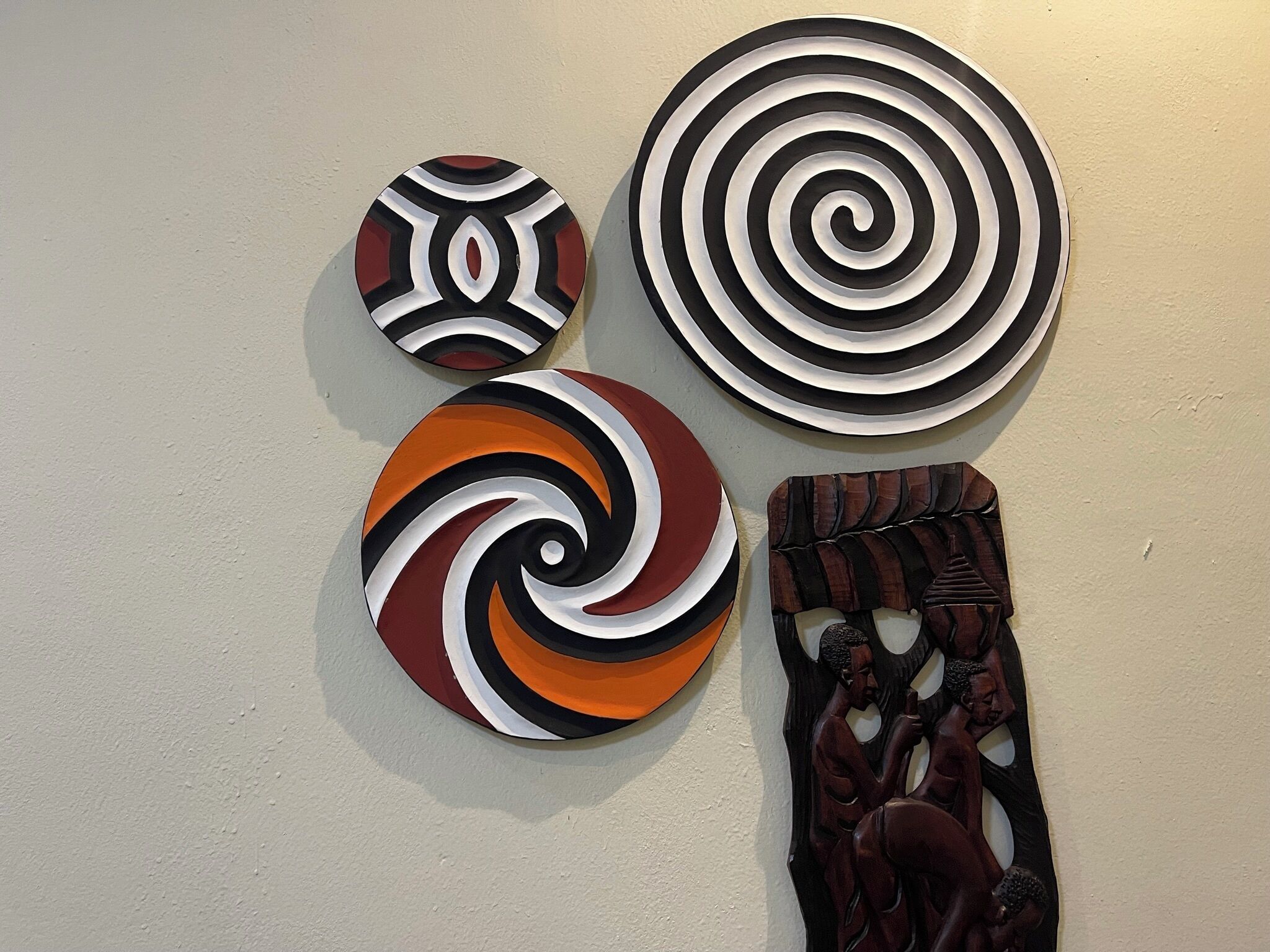 Cuatro obras de arte colgantes con diseños abstractos y una escultura de madera.