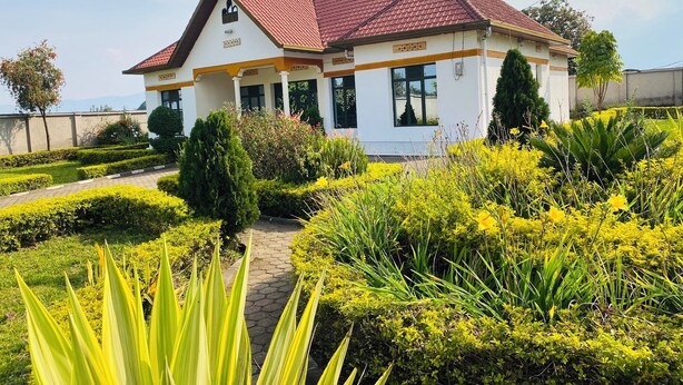 A two-story house with a red-tiled roof, surrounded by well-maintained gardens and a paved pathway. - Virunga House (Muhoza)