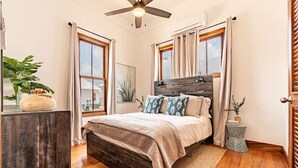 A bedroom with a bed, wooden floor, ceiling fan, windows, curtains, and a small side table. - The Weekender & Mistico Beach Club + Boat Shuttle (San Pedro)