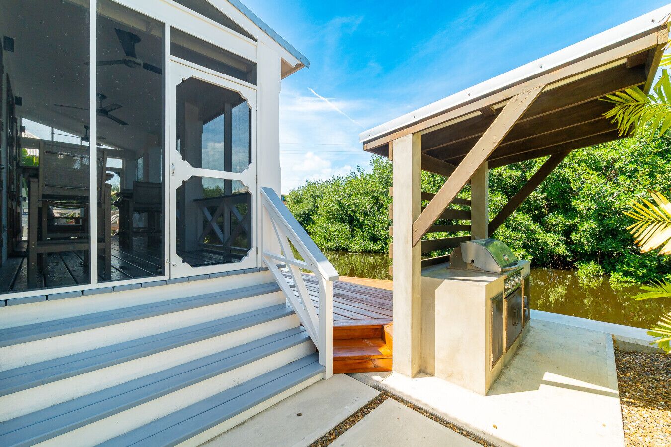 Ein Wohnhaus am Wasserufer mit einer überdachten Terrasse, einer Treppe zu einer überdachten Veranda und Blick auf das Wasser.