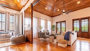 A spacious living area with wooden flooring, a sofa, a chair, a coffee table, and a large window. - The Weekender & Mistico Beach Club + Boat Shuttle (San Pedro)