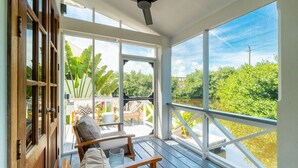 A covered porch with a ceiling fan, large windows, and a view of greenery and water. - The Weekender & Mistico Beach Club + Boat Shuttle (San Pedro)