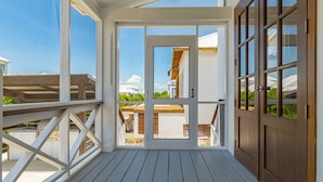 Un espace extérieur abrité doté d’une terrasse en bois, de rampes blanches et offrant une vue sur un bâtiment surmonté d’un dôme blanc et d’un toit en bois.