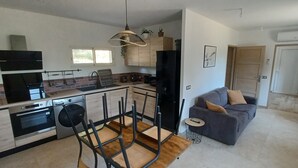 A modern kitchen with a dining area, a grey sofa, and a wooden table.