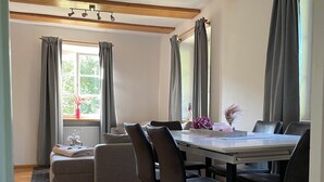 Zona pranzo con tavolo in legno, sedie nere e divano grigio.