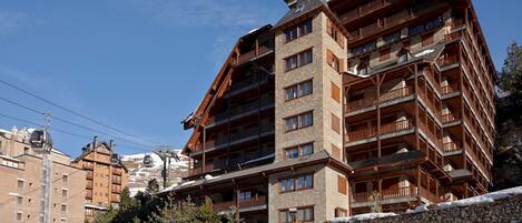 A multi-story hotel with a stone facade, wooden balconies, and a ski lift in the background.