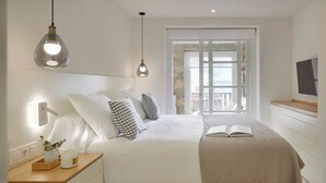 A modern bedroom with a large bed, bedside tables, a TV, and a window with a view. - Port Luxe by FeelFree Rentals (Baqueira)