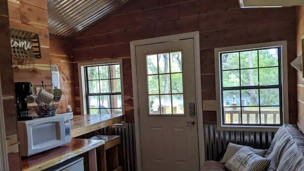 Interior acolhedor de uma cabana com decoração em madeira, uma kitchenette, uma porta e janelas amplas.