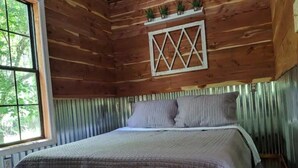 Quarto de cabana de madeira, com cama, janela e painel decorativo em madeira acima da cama.
