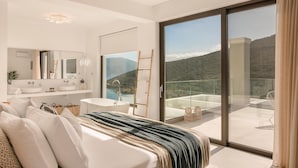 A modern bedroom with a large bed, a bathroom with a bathtub, and a balcony with a mountain view.