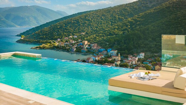 A luxurious infinity pool with a clear view of a coastal village and mountains in the background.