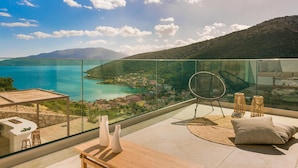 A balcony with a glass railing overlooking a coastal town and mountains.