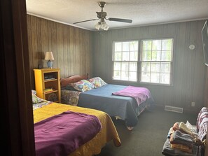 A bedroom with two beds, a ceiling fan, a window with blinds, and a bookshelf.