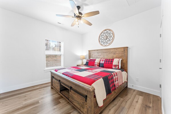 A bedroom with a wooden bed, a ceiling fan, a decorative wall piece, and a window with blinds. - Breathtaking Scenery and Plenty of Room to Enjoy Time with the Whole Family! (Branson)