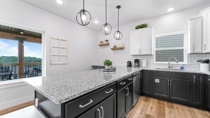 A modern kitchen with granite countertops, black cabinets, and pendant lighting.