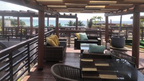A covered outdoor seating area with wicker furniture, a table, and a view of the ocean. - Aldea Thai penthouse 307 ocean view  (Playa del Carmen)