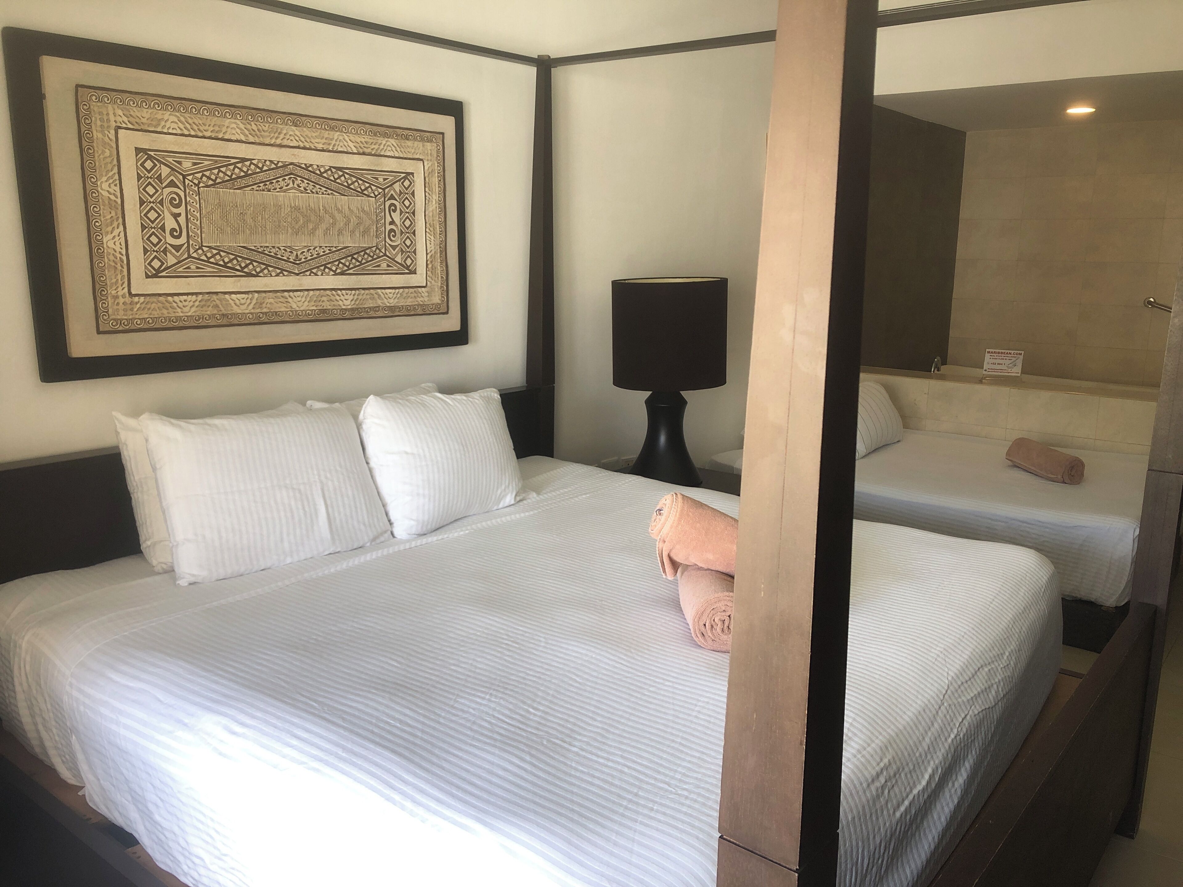 A hotel room with a large bed, a bedside table with a lamp, a bathroom with a bathtub, and a framed artwork on the wall.