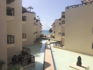 Ett semesterhotell med en central pool, flera balkonger och utsikt över havet.