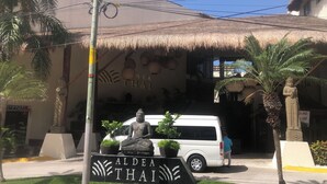 A building with a sign reading "ALDEA THAI" and a statue in front.