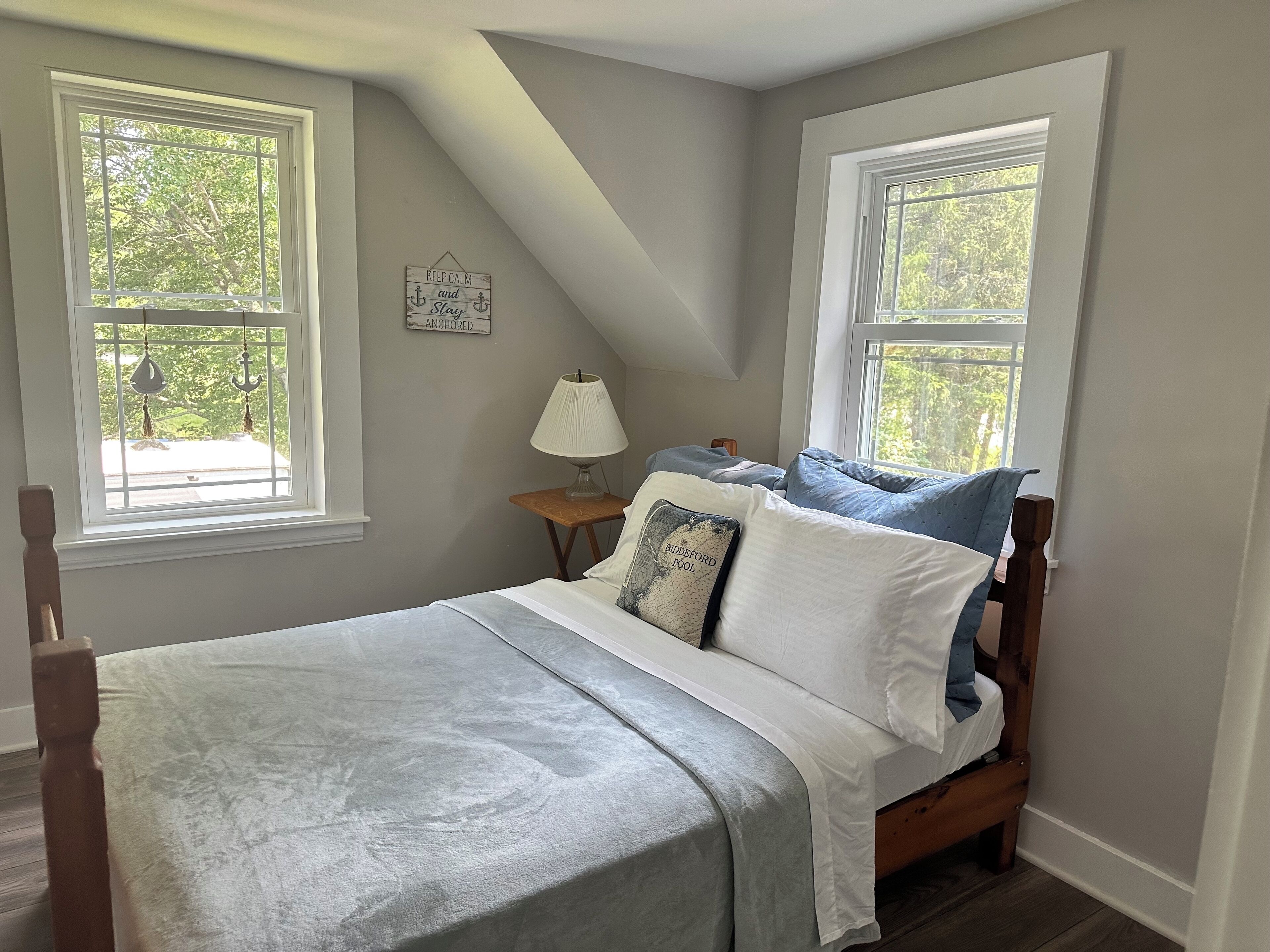 A bedroom with a bed, two windows, a nightstand, and a lamp.