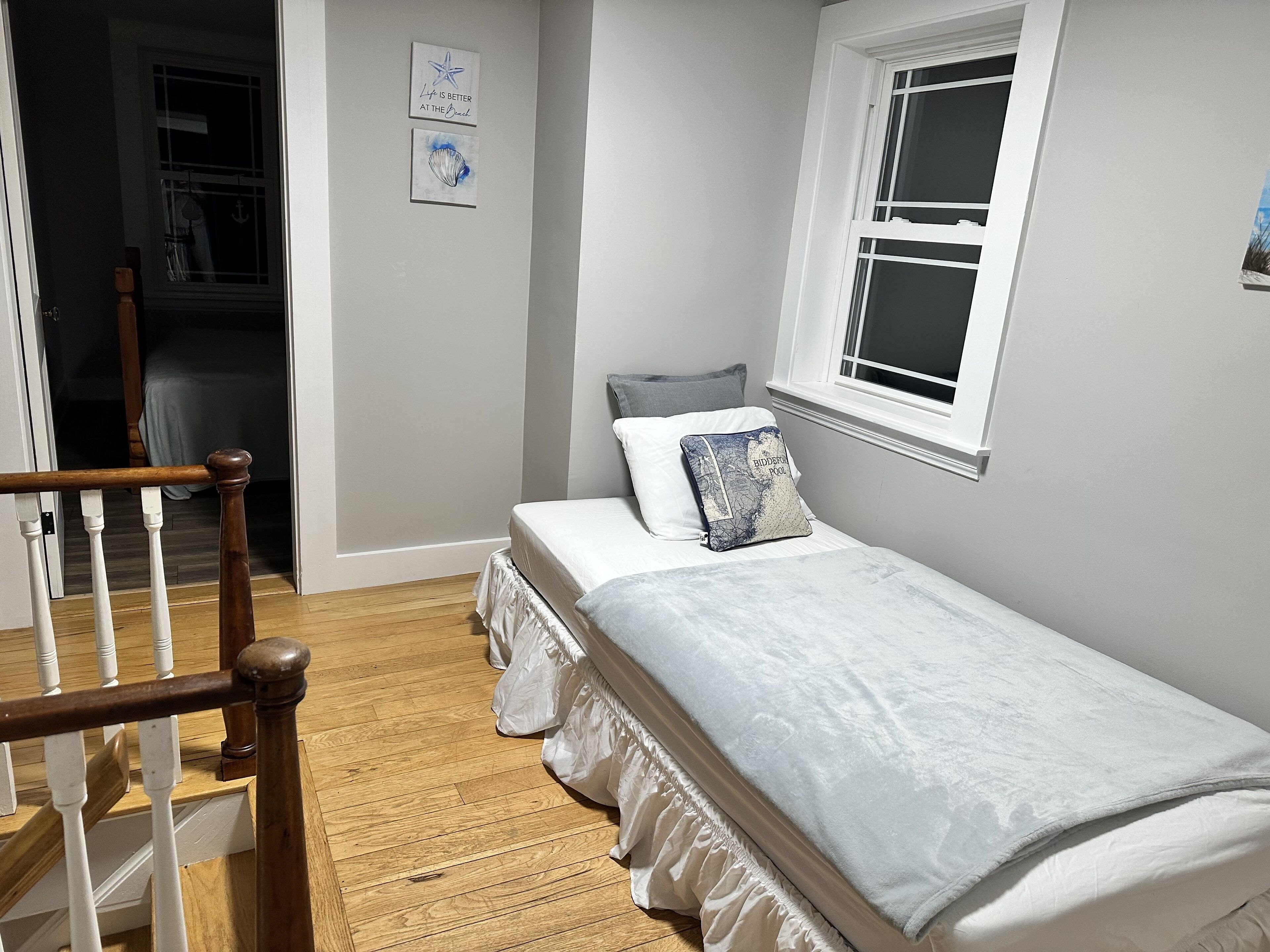A bedroom with a bed, a window, a wooden staircase, and a door leading to another room.